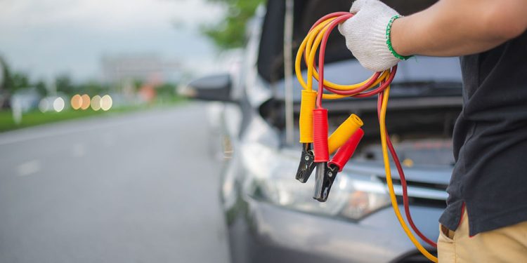 Young man charging battery car with electricity trough jumper cables on the country road,copy space.insurance and service concept.